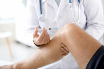 A doctor injecting into a patient's knee joint.
